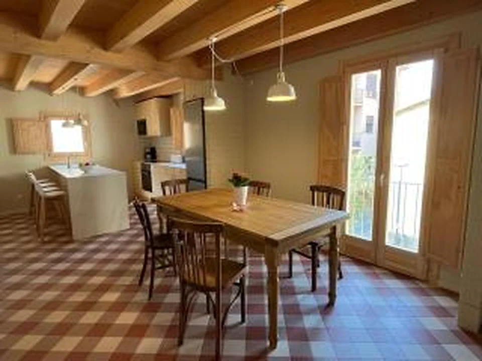 Taula extensible de fusta en primer pla i cuina de Can Fèlix al fons